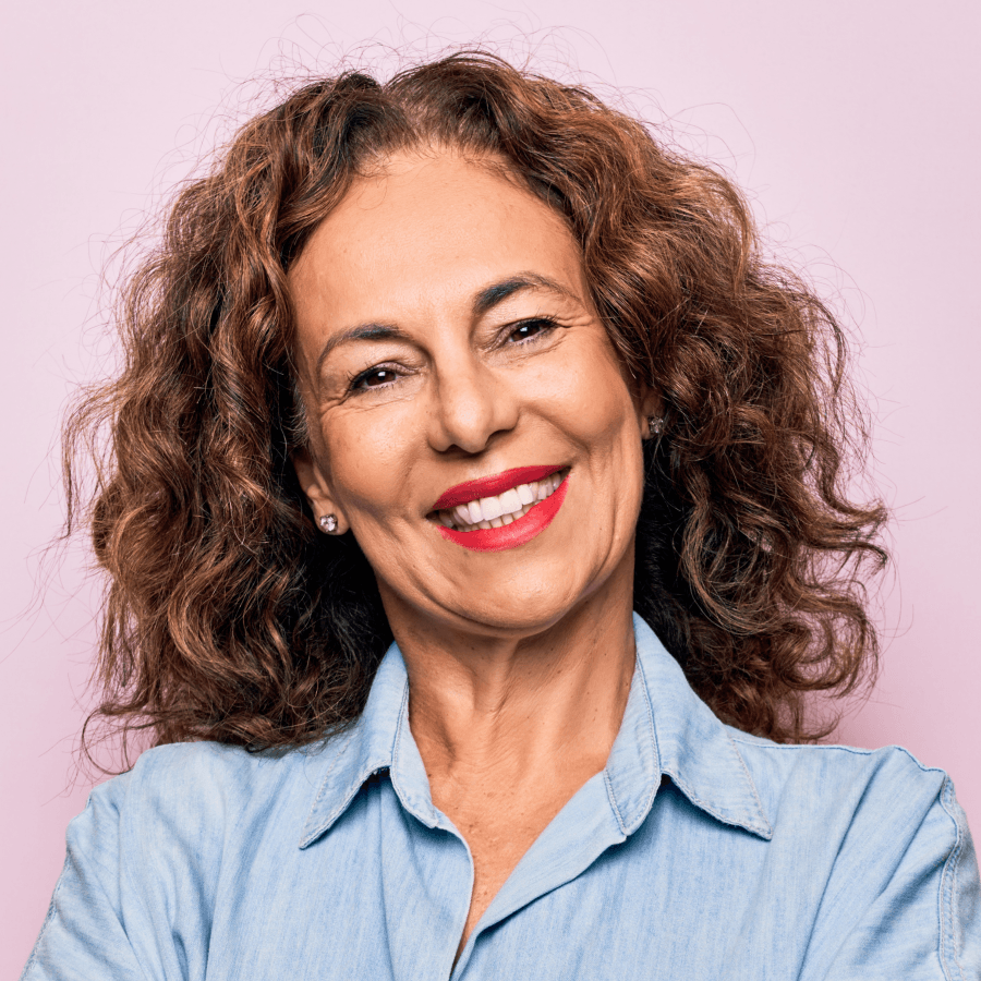 Mulher branca, de cabelos castanhos cacheados, sorrindo com batom vermelho e camisa azul claro.